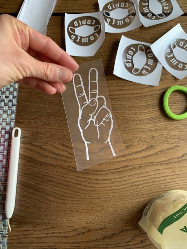 photo of Brittany Wells holding a decal of a hand making a peace sign with other craft materials and decals in the background